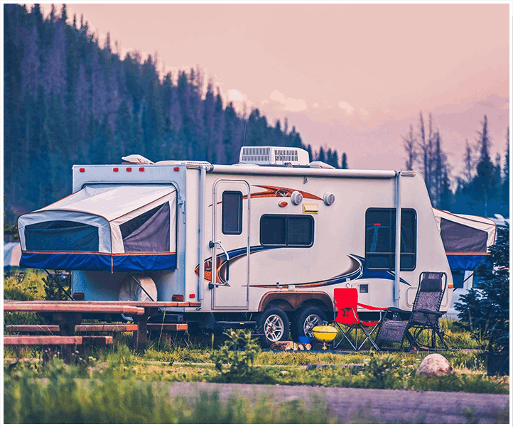 A white rv parked in the grass near some trees.