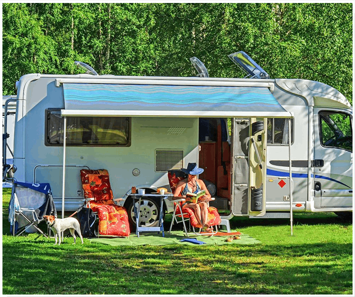 A woman sitting outside of her rv with two dogs.